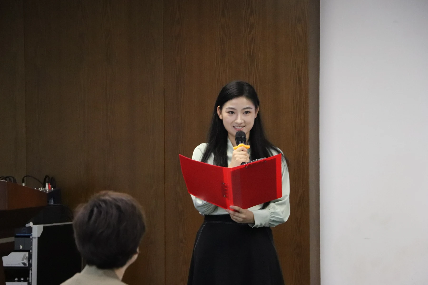 Huiyao hosting a camp event with a microphone and red script folder